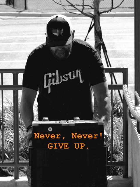 Band member behind equipment marked Never, Never Give Up